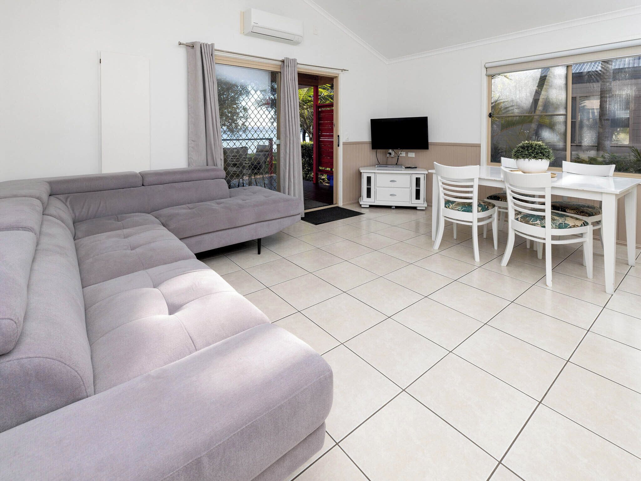 Una sala de estar moderna con un sofá seccional gris, una mesa de comedor con sillas, un televisor y un mueble bajo.