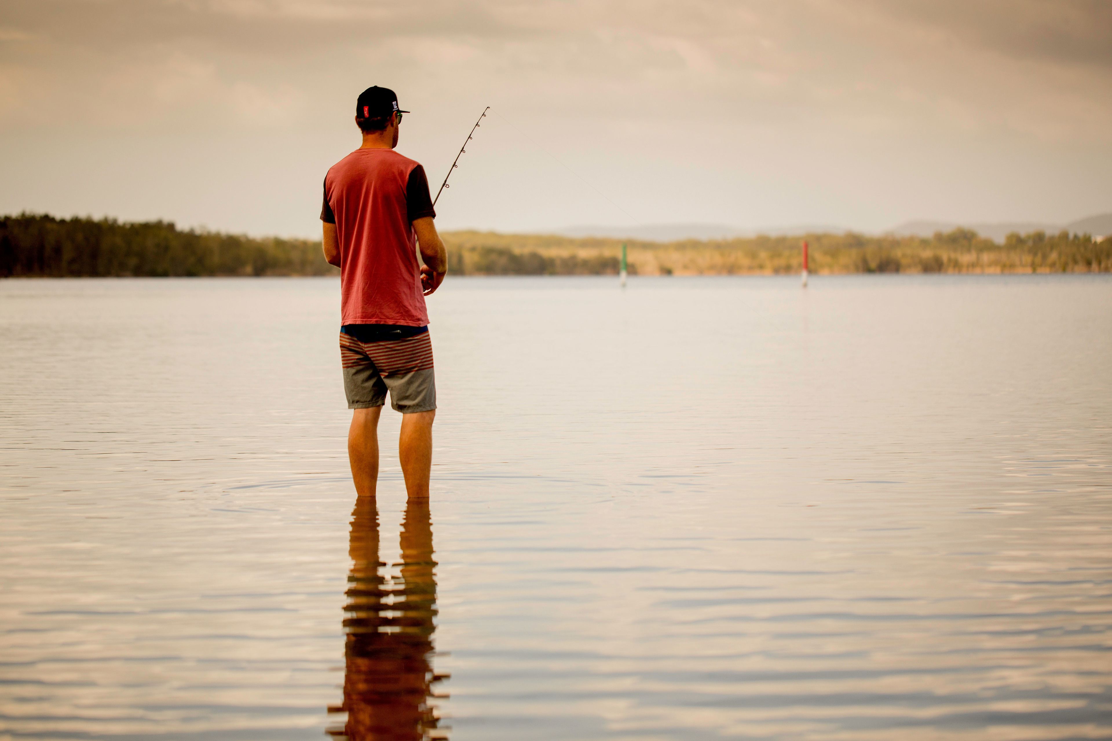 A man standing in a calm lake holding a fishing rod.