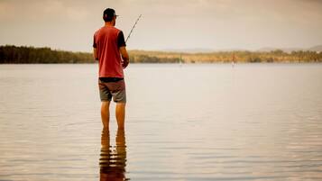 Un hombre de pie en un lago tranquilo sosteniendo una caña de pescar.