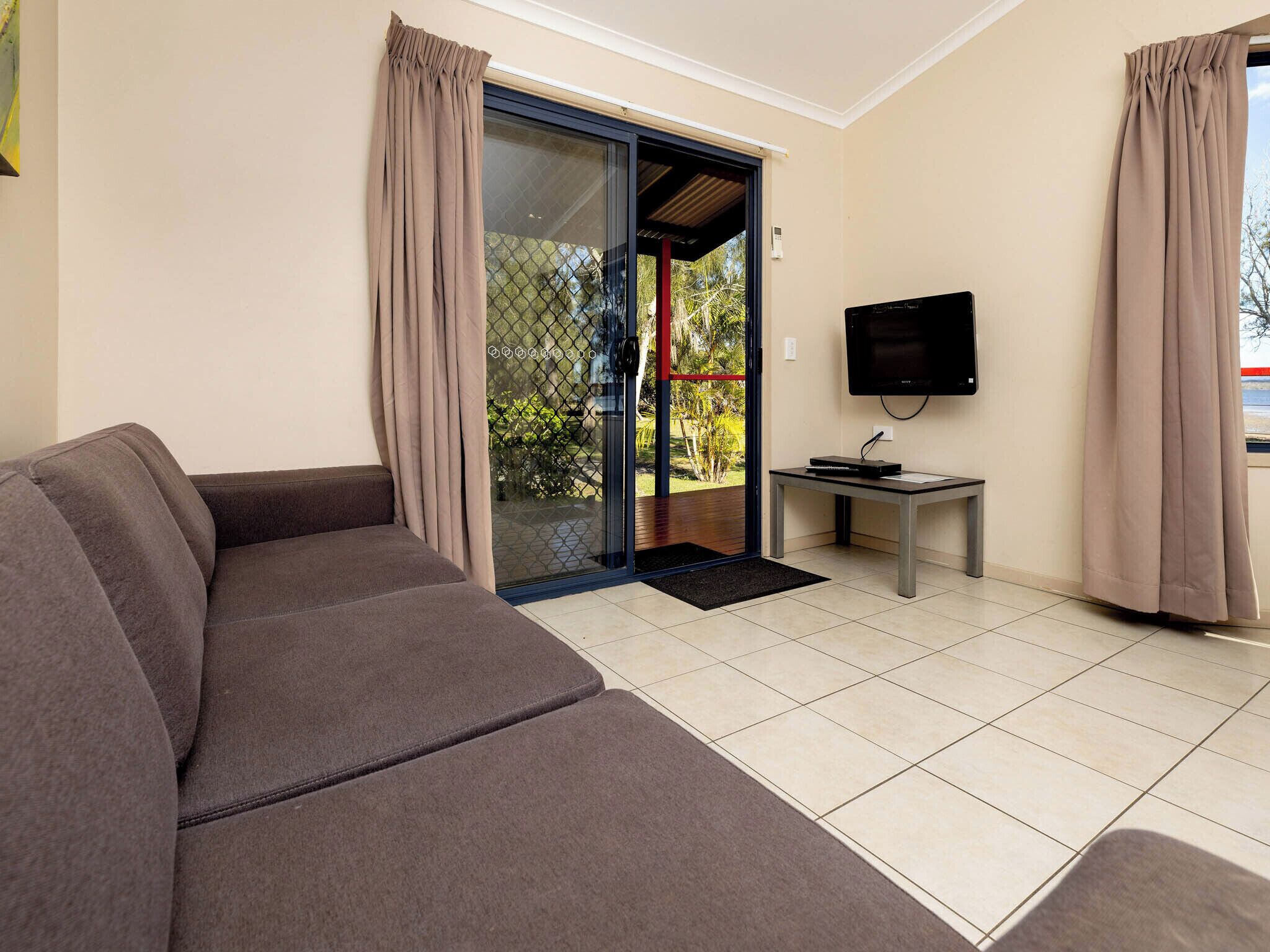 A living room with a sofa, a television on a stand, and a sliding glass door leading to a balcony.