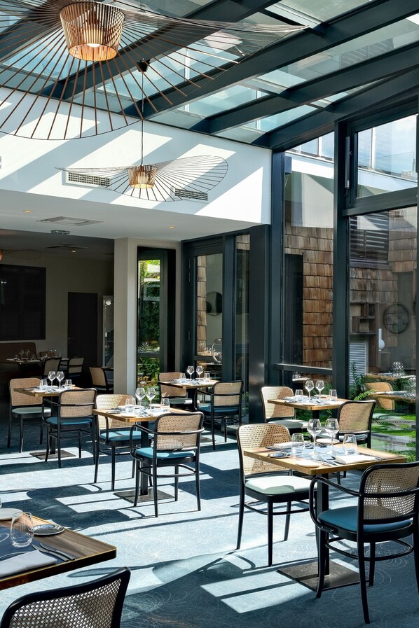An outdoor dining area with tables and chairs, large windows, and a modern ceiling design.
