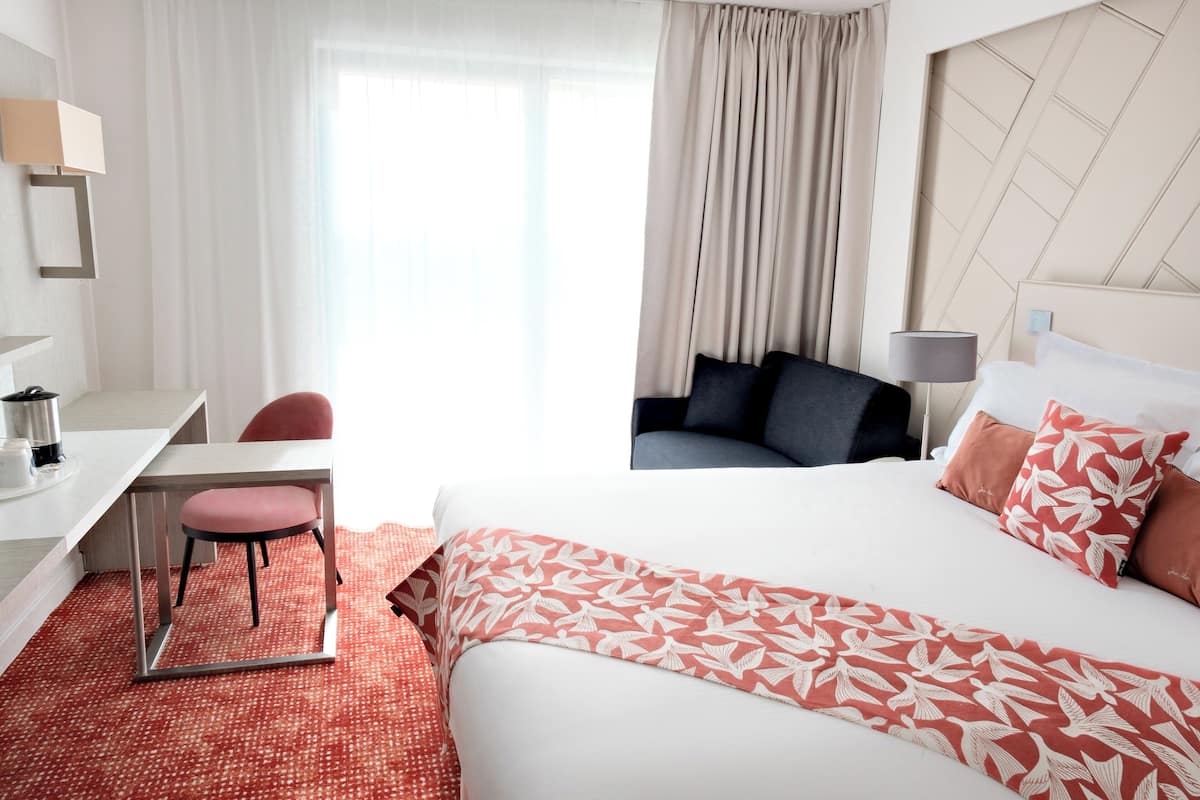 A hotel room with a bed, a desk, a chair, and a sofa.