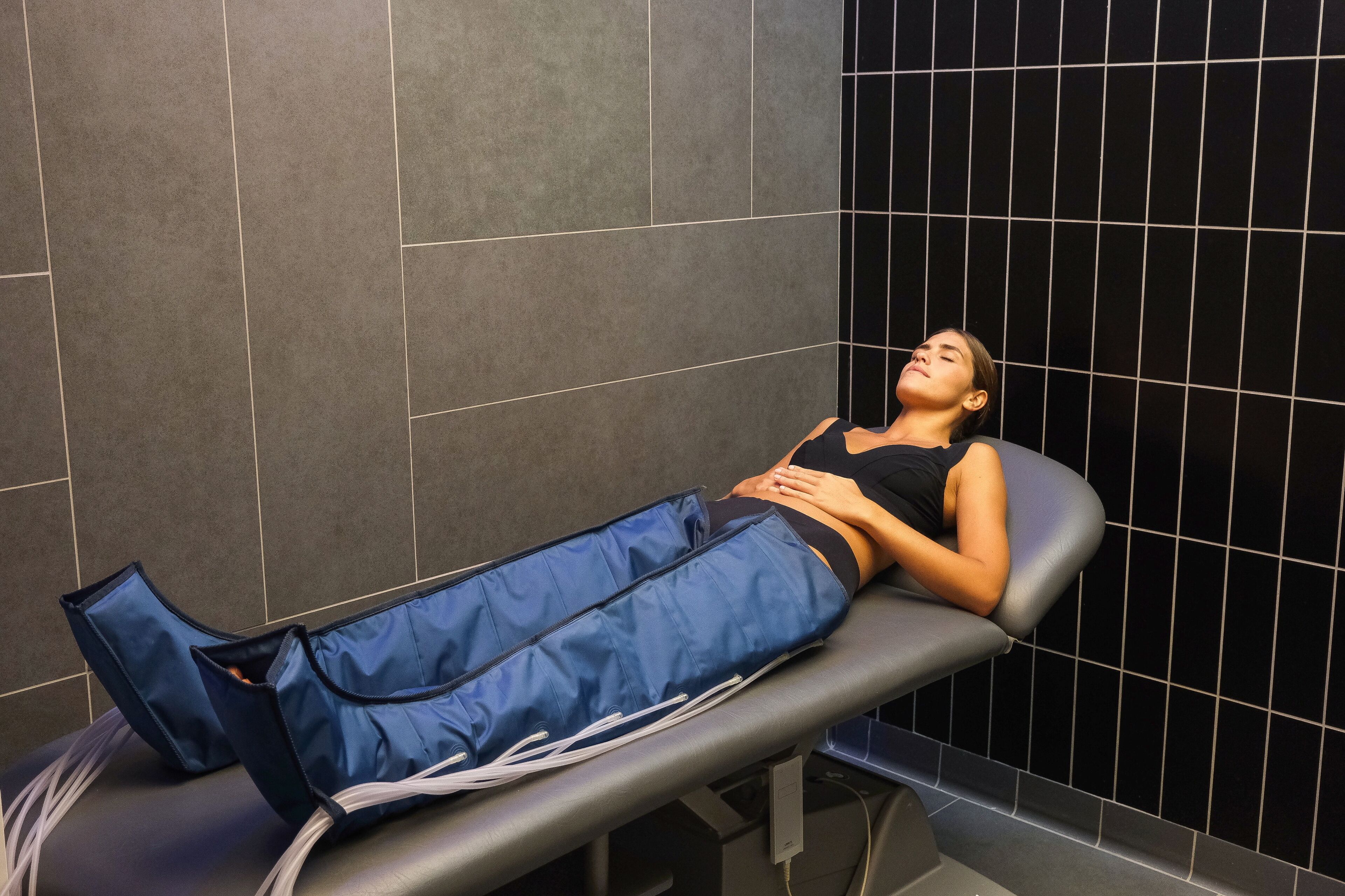 En person ligger på ett massagebord i ett rum med mörka, kaklade väggar.