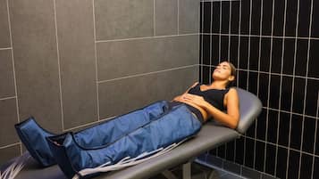 Iemand ligt op een massagetafel in een ruimte met donkere betegelde muren.