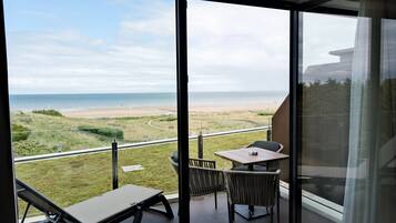 A balcony with a view of the beach, a table, and two chairs.