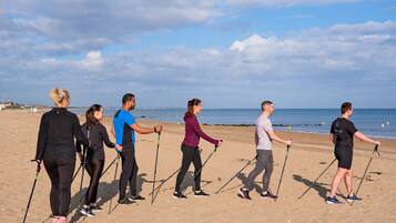Un groupe de personnes se promène sur une plage de sable, avec un ciel dégagé et l’océan en arrière-plan.