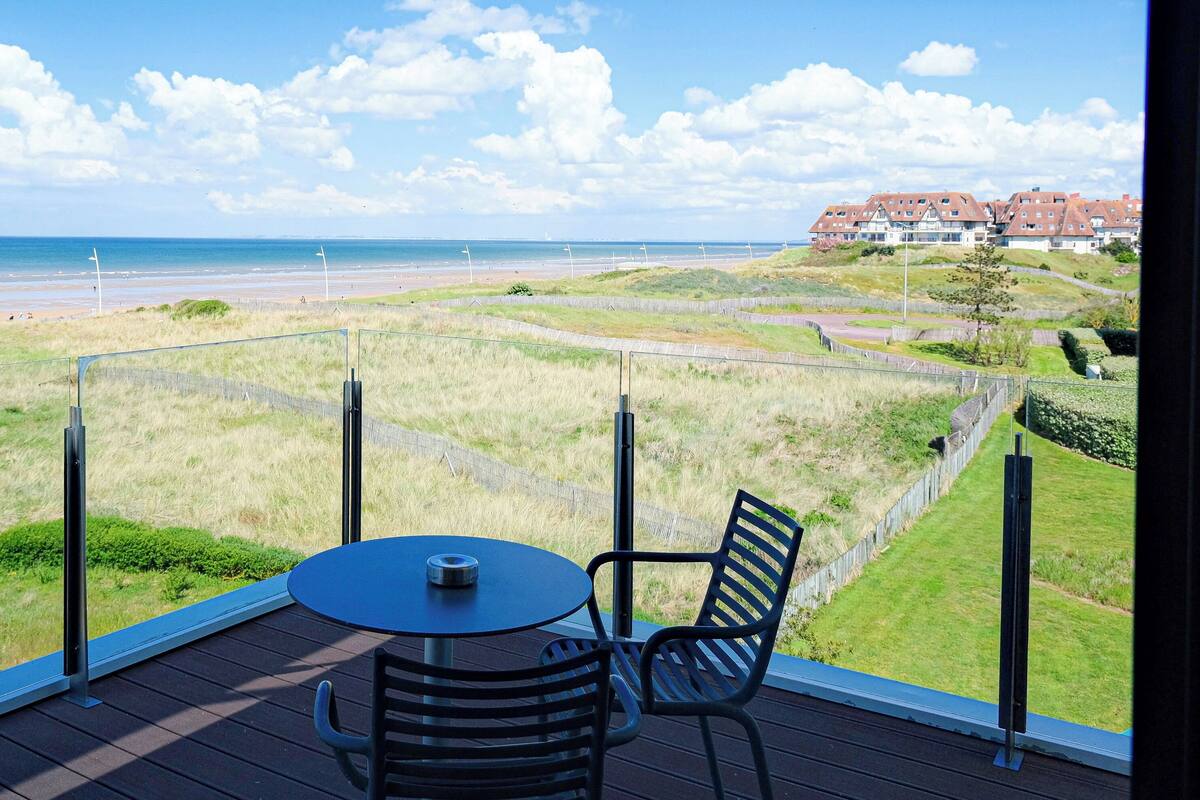 A balcony with a table and chairs overlooking a beach and a residential area.