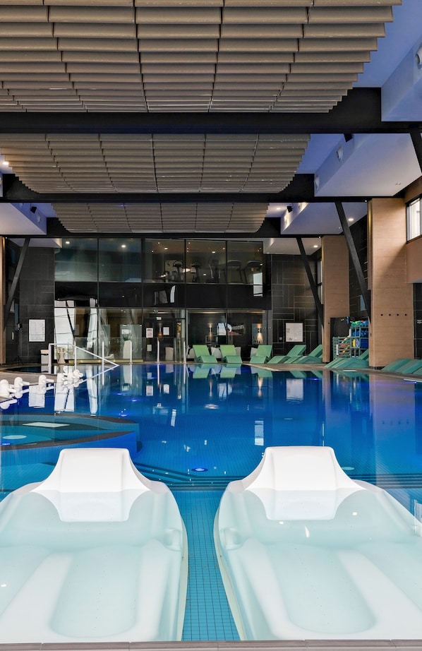 Una piscina interior con agua cristalina, sillones de descanso y un diseño arquitectónico moderno.