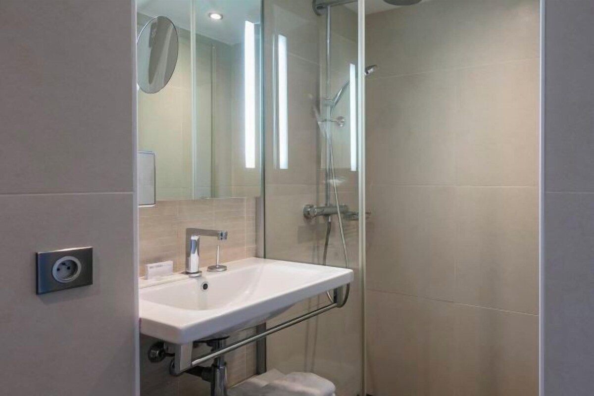 Ein modernes Badezimmer mit einer Duschkabine aus Glas, einem weißen Waschbecken und einem Spiegel.