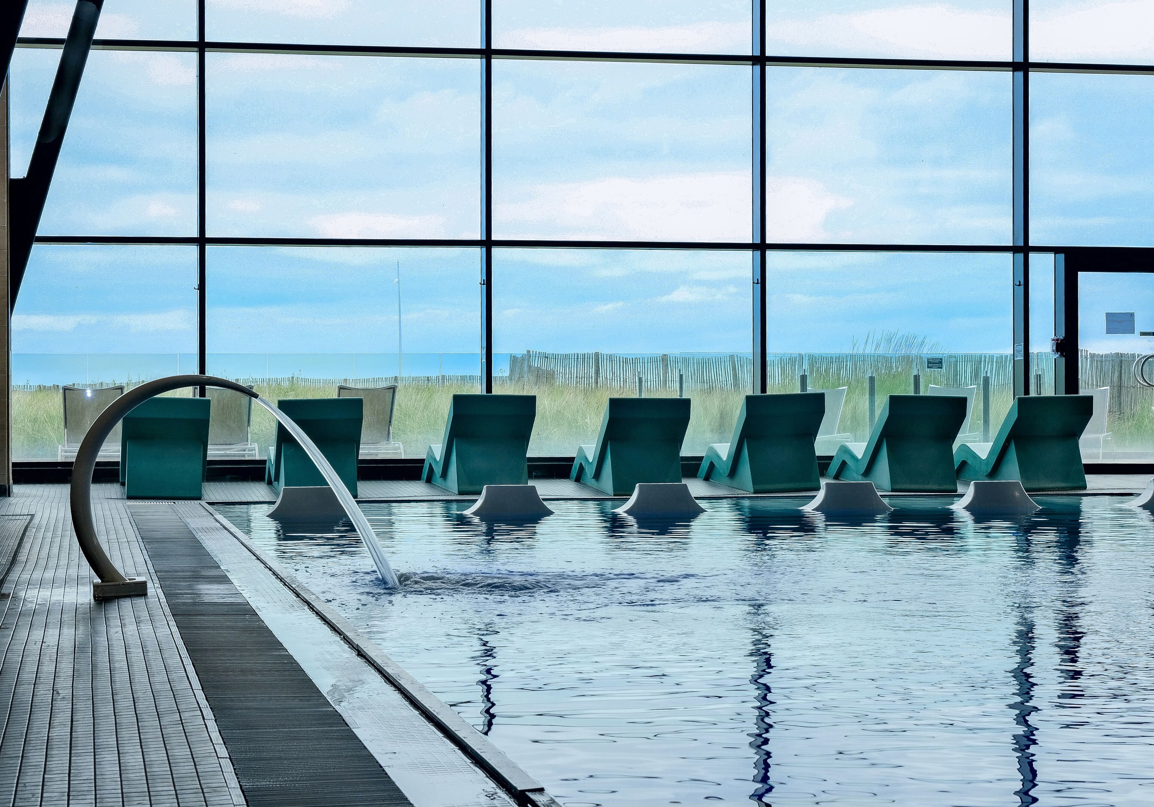 A swimming pool with clear blue water, surrounded by green chairs and a wooden deck.