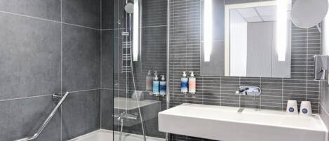 A modern bathroom with a glass-enclosed shower, a white sink with two soap dispensers, and a large mirror.