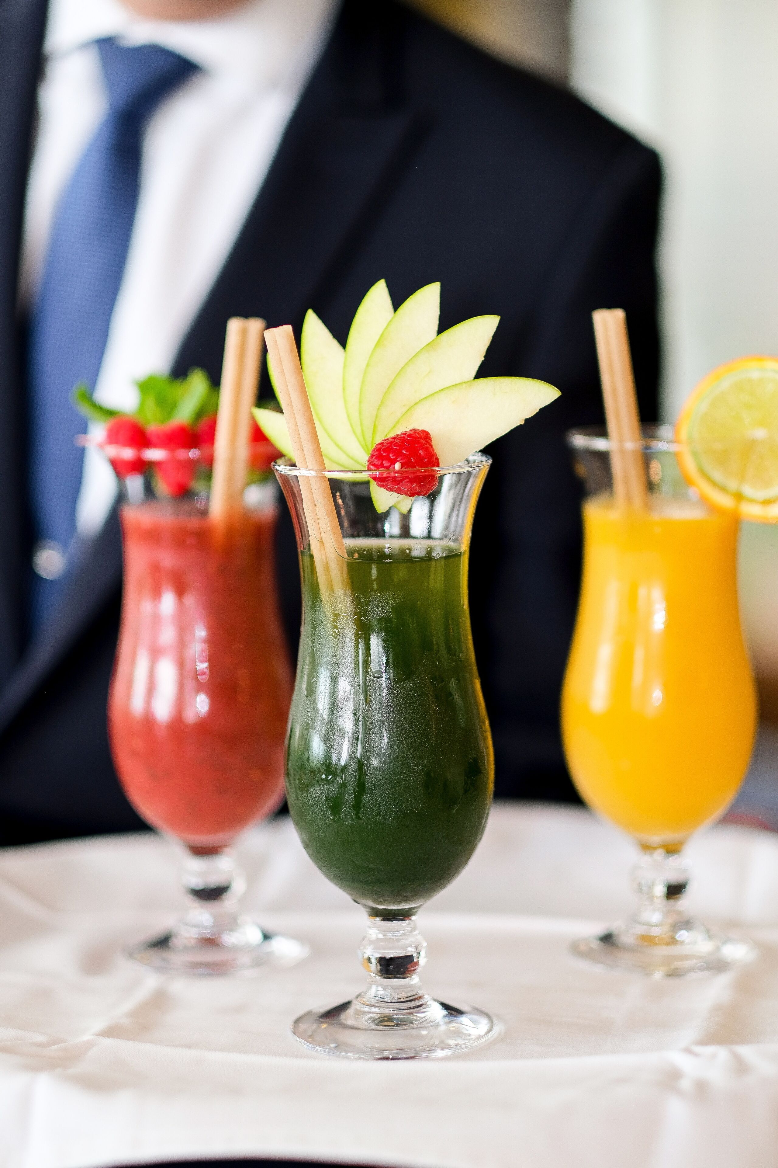 Tres cócteles en vasos con pajitas, adornados con rodajas de fruta y una fresa.