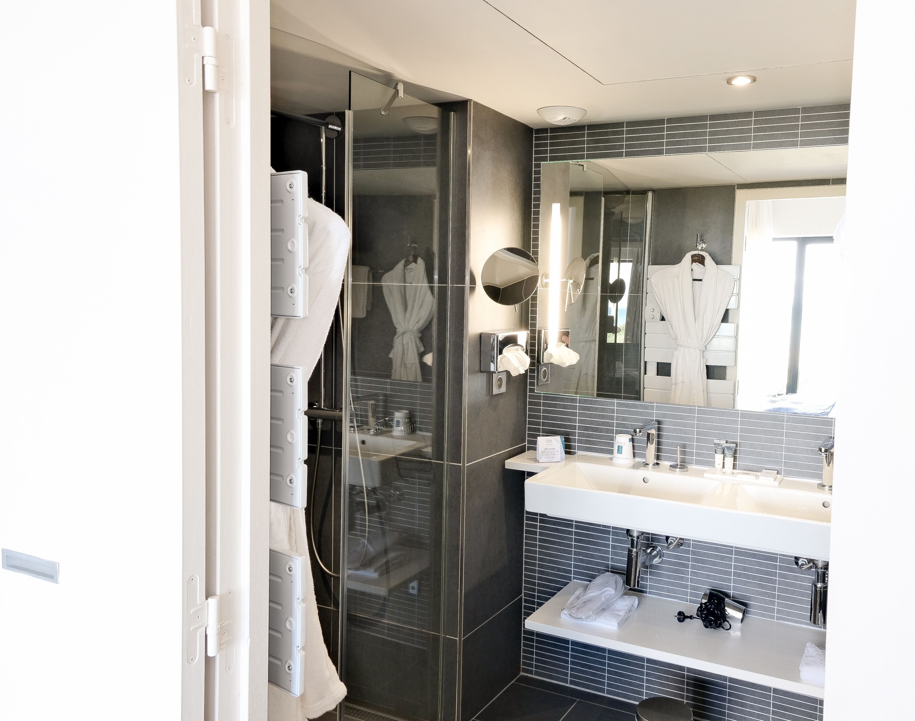 A modern bathroom with a glass shower enclosure, a large mirror, and a white sink with a towel.