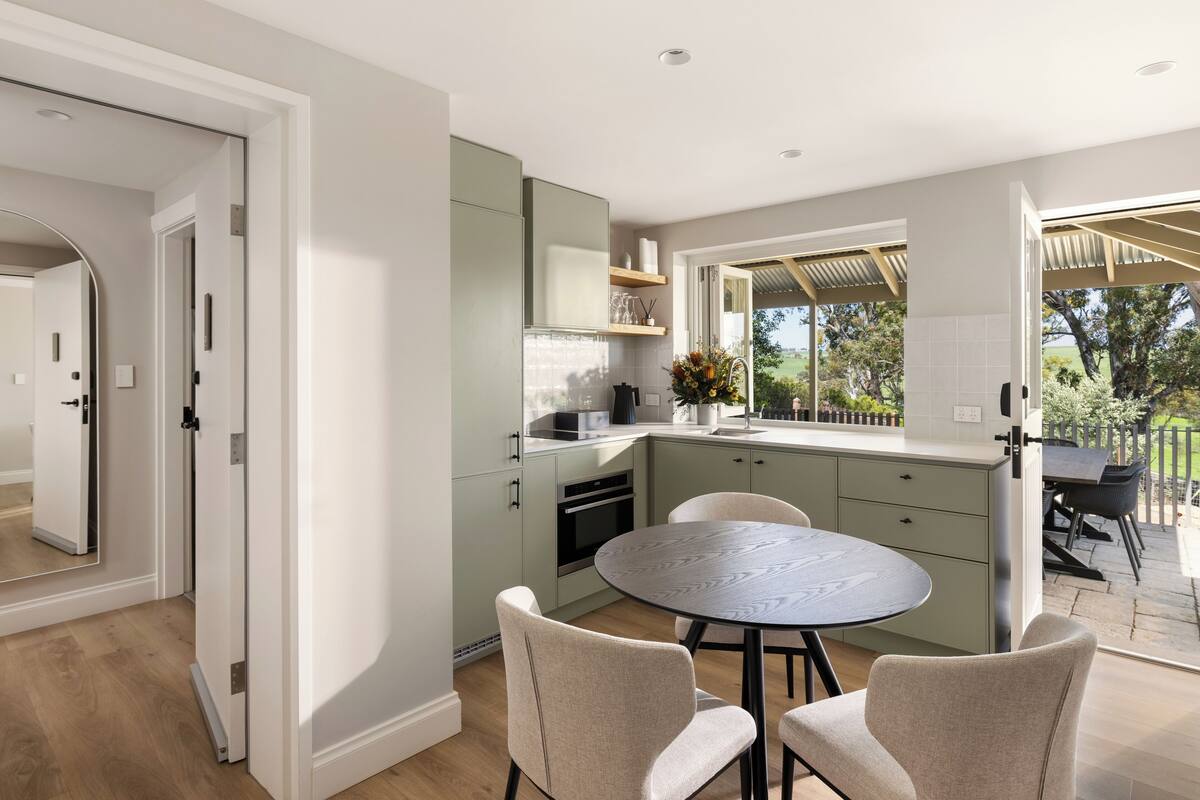 A modern kitchen with a round dining table and chairs, light green cabinets, and a view of the outdoors.