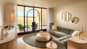 Un moderno salón con un amplio ventanal corredera que da a un espacio exterior, un sofá verde, un reposapiés redondo y una mesita de madera con una vela.