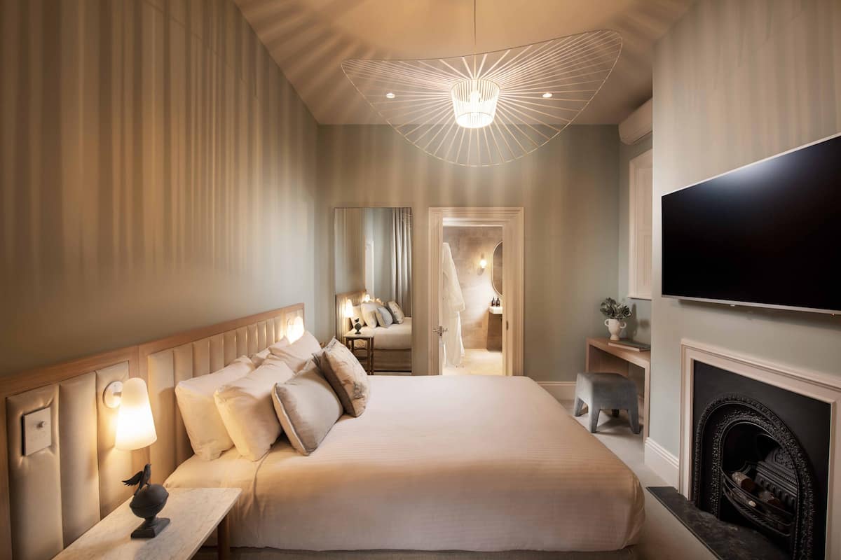 A hotel bedroom with a large bed, bedside lamps, a television, and a fireplace.