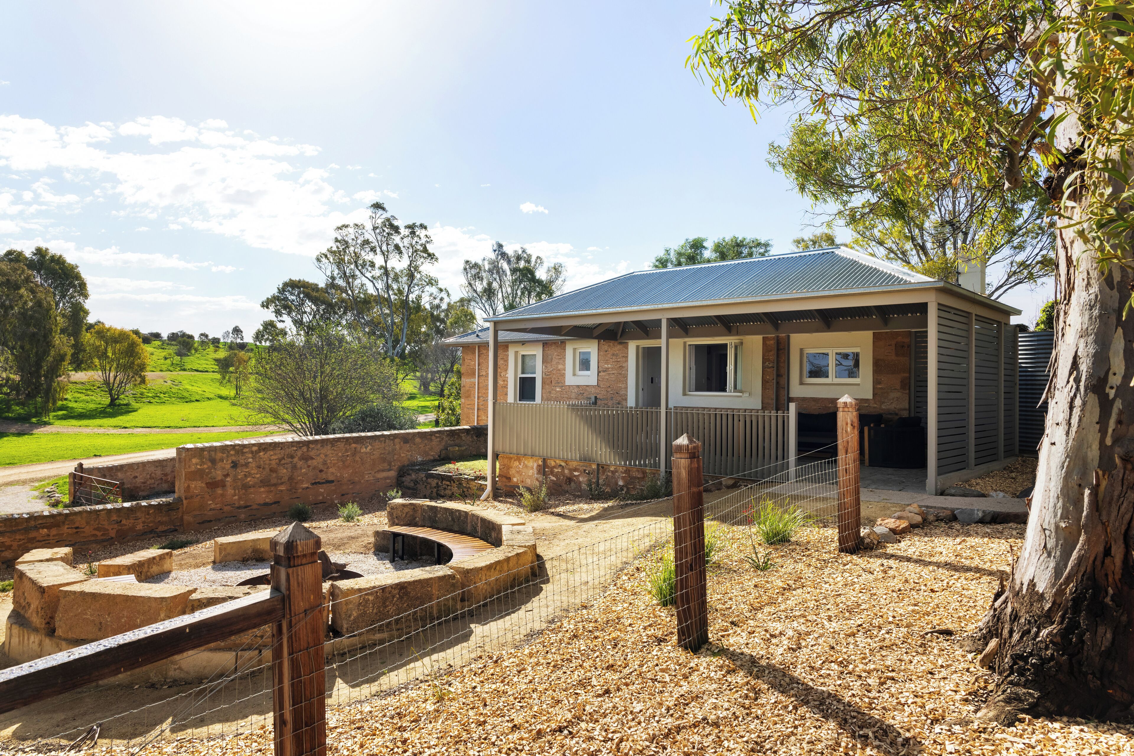 A building with a brick facade, a covered porch, and a fenced outdoor area with steps leading to a water feature.