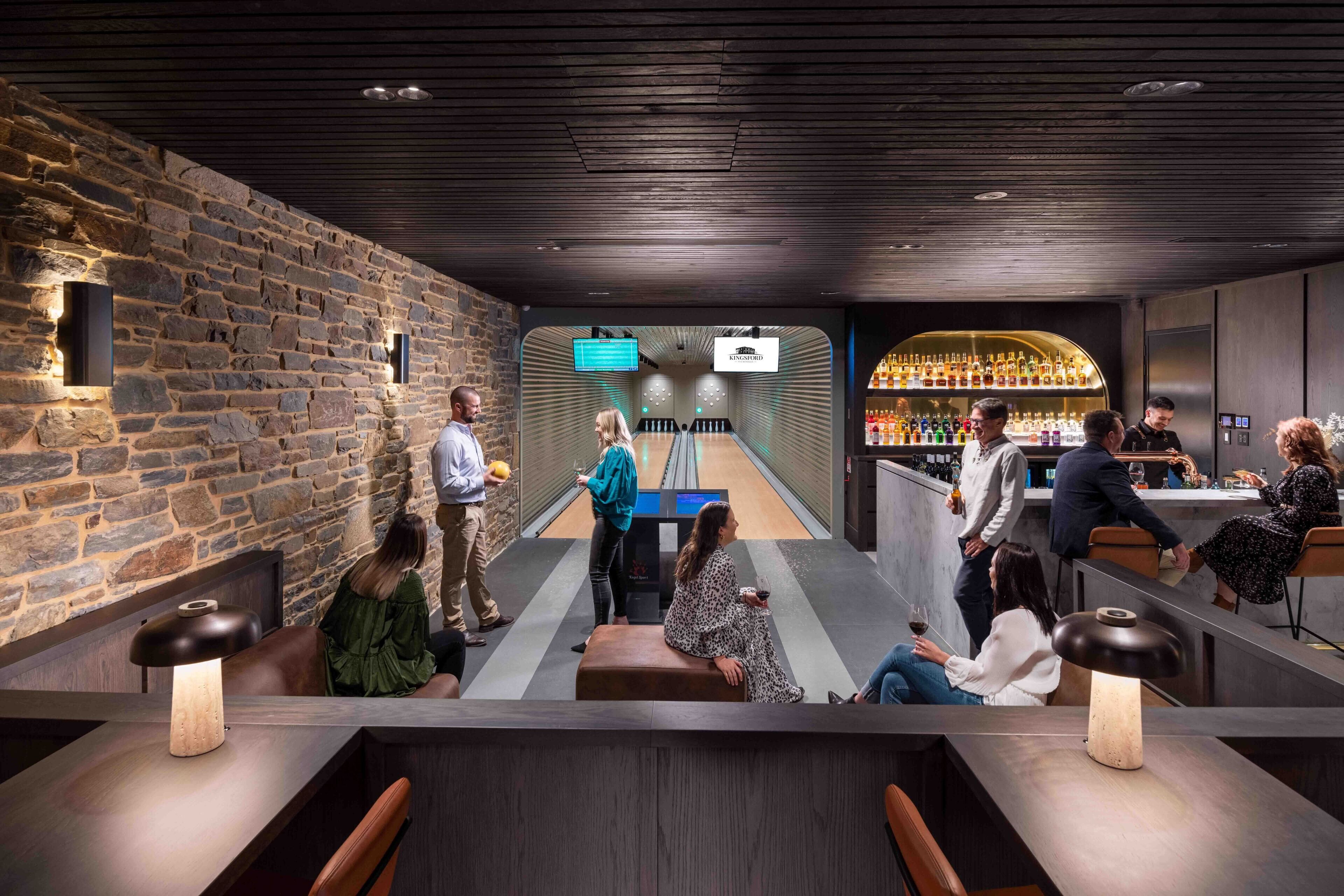 A modern bar area with stone walls, seating, and a bowling lane.
