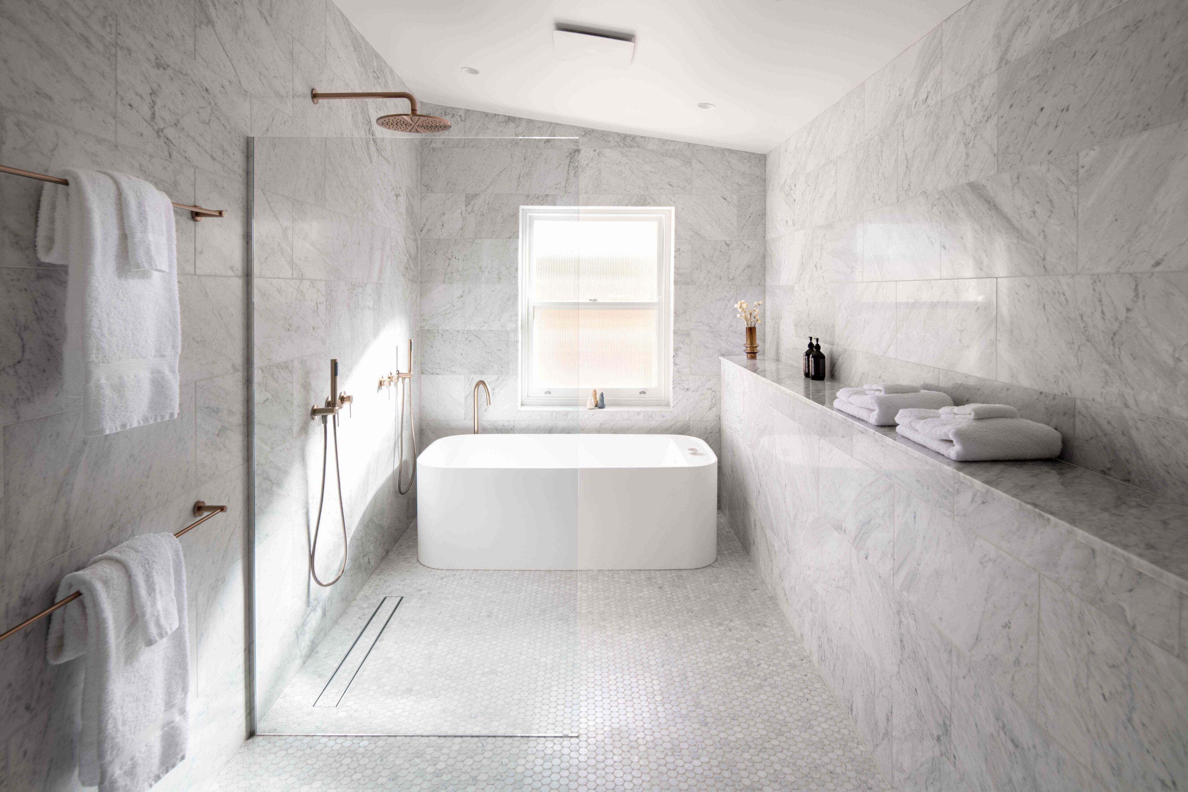 A modern bathroom with a freestanding bathtub, a glass-enclosed shower, and marble walls.