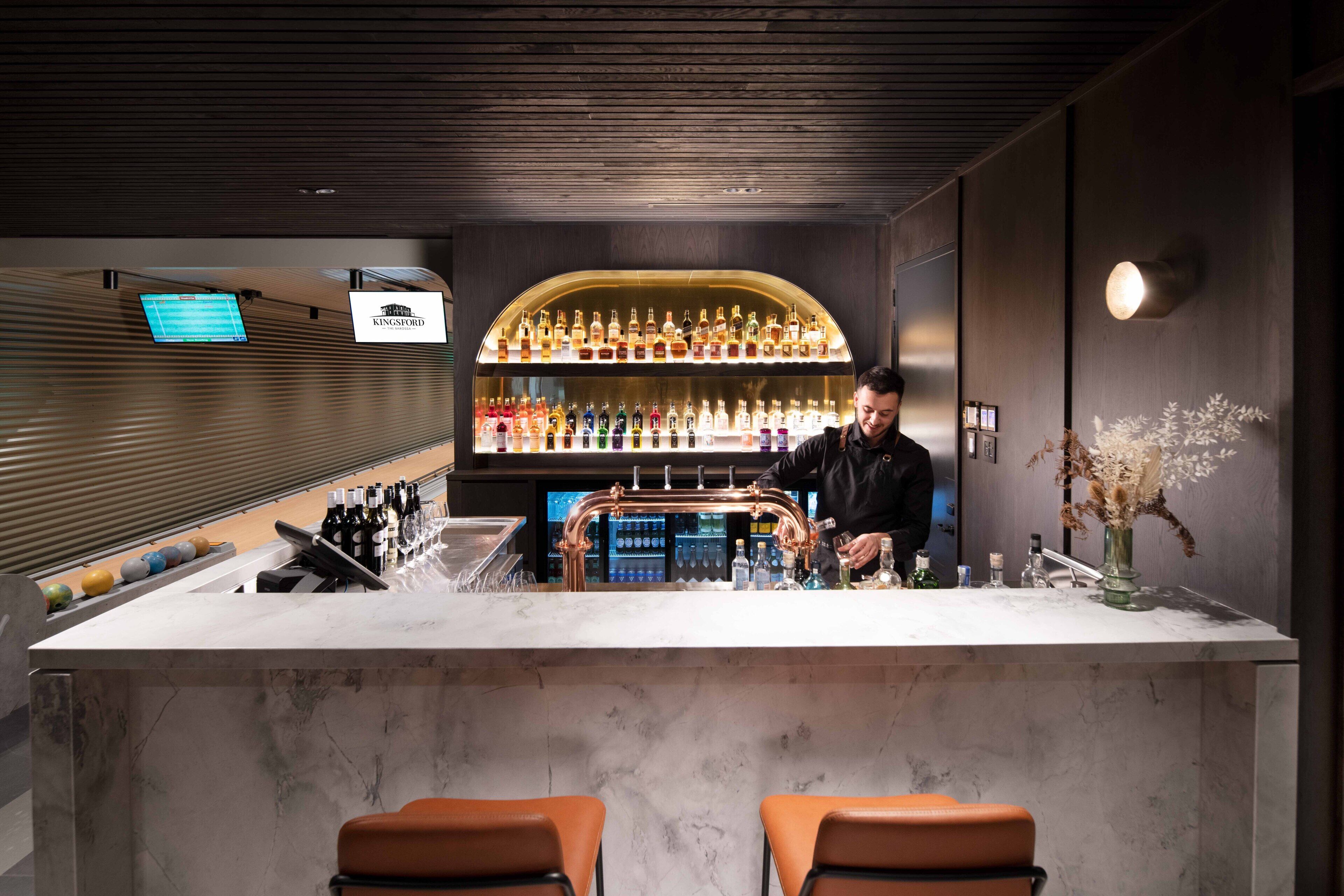 A bar area with a bartender, a marble counter, and a shelf of bottles.