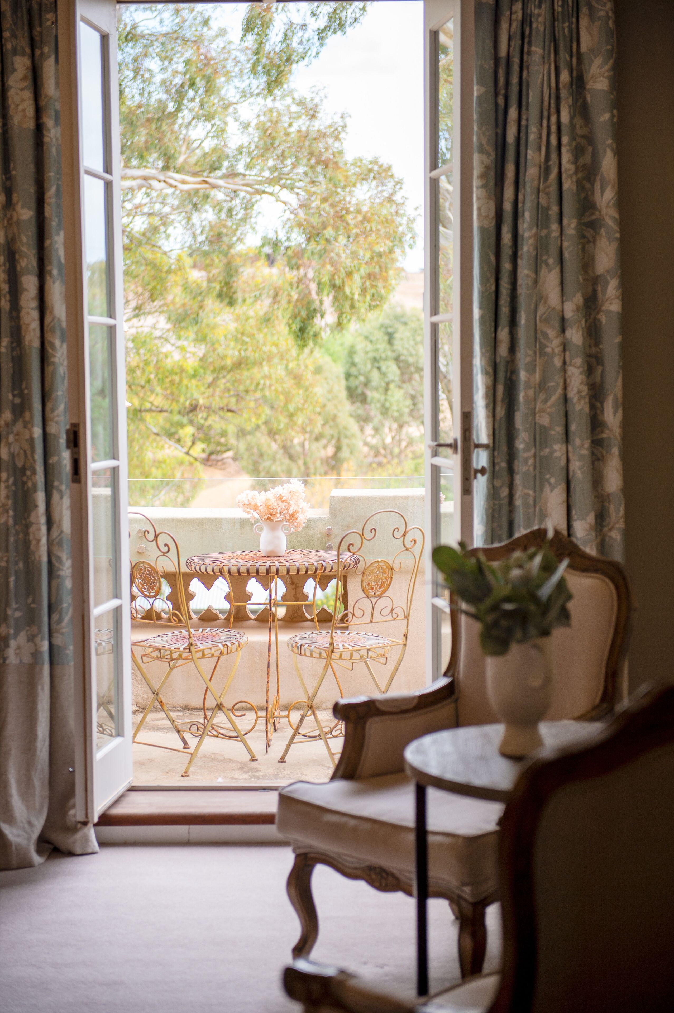 A room with a balcony, a table with chairs, and a potted plant.