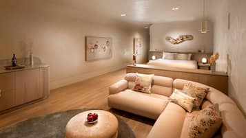 Un dormitorio moderno con un sofá, un reposapiés redondo con fruta, una cama y obras de arte en las paredes.