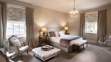 A bedroom with a large bed, two bedside tables with lamps, a chair, an ottoman, and a chandelier.