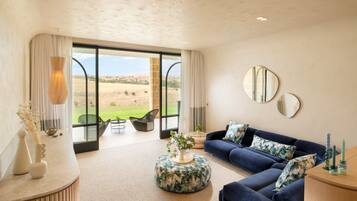 A spacious living room with a large window, a blue sofa, and a round ottoman.