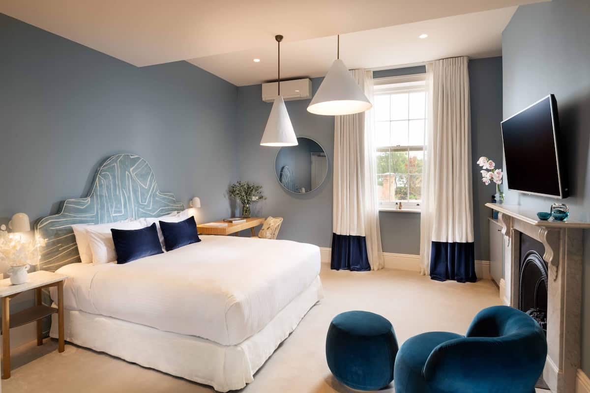 A modern bedroom with a large bed, two pendant lights, a flat-screen TV, a fireplace, and a view of the outdoors.