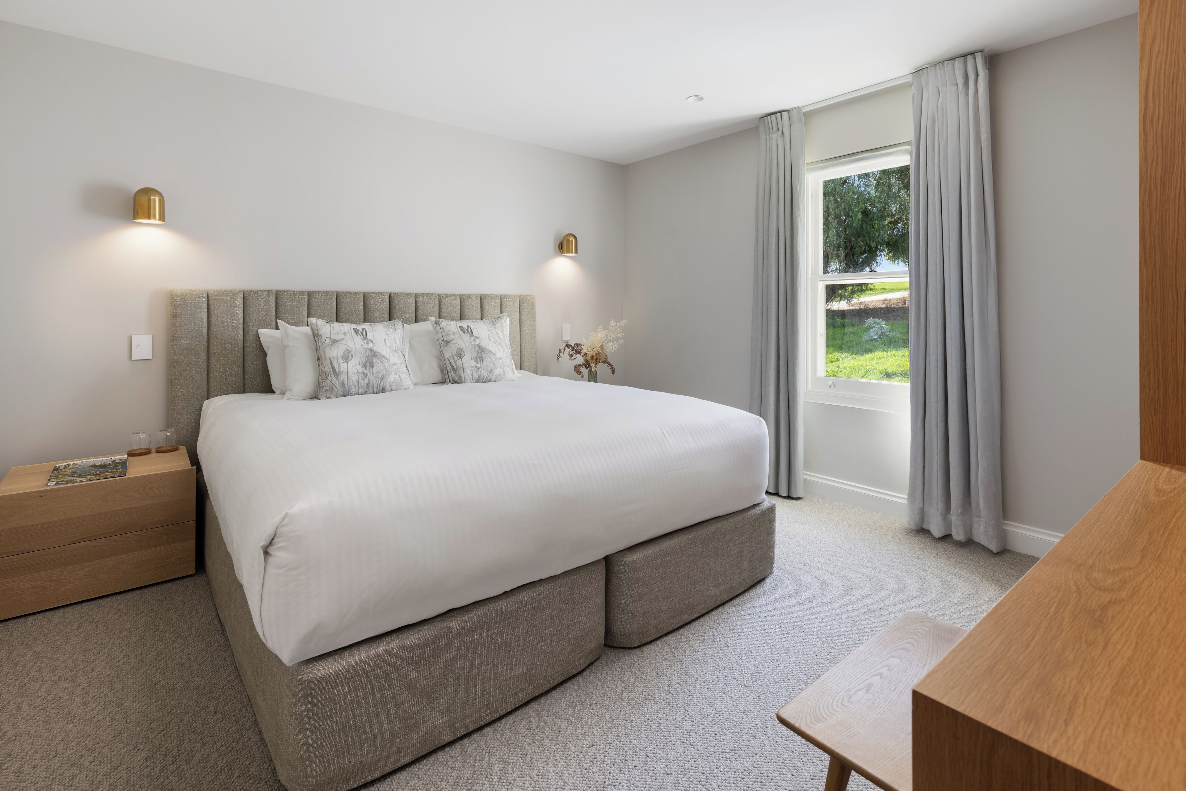 A modern bedroom with a large bed, bedside tables, and a view of the outdoors.