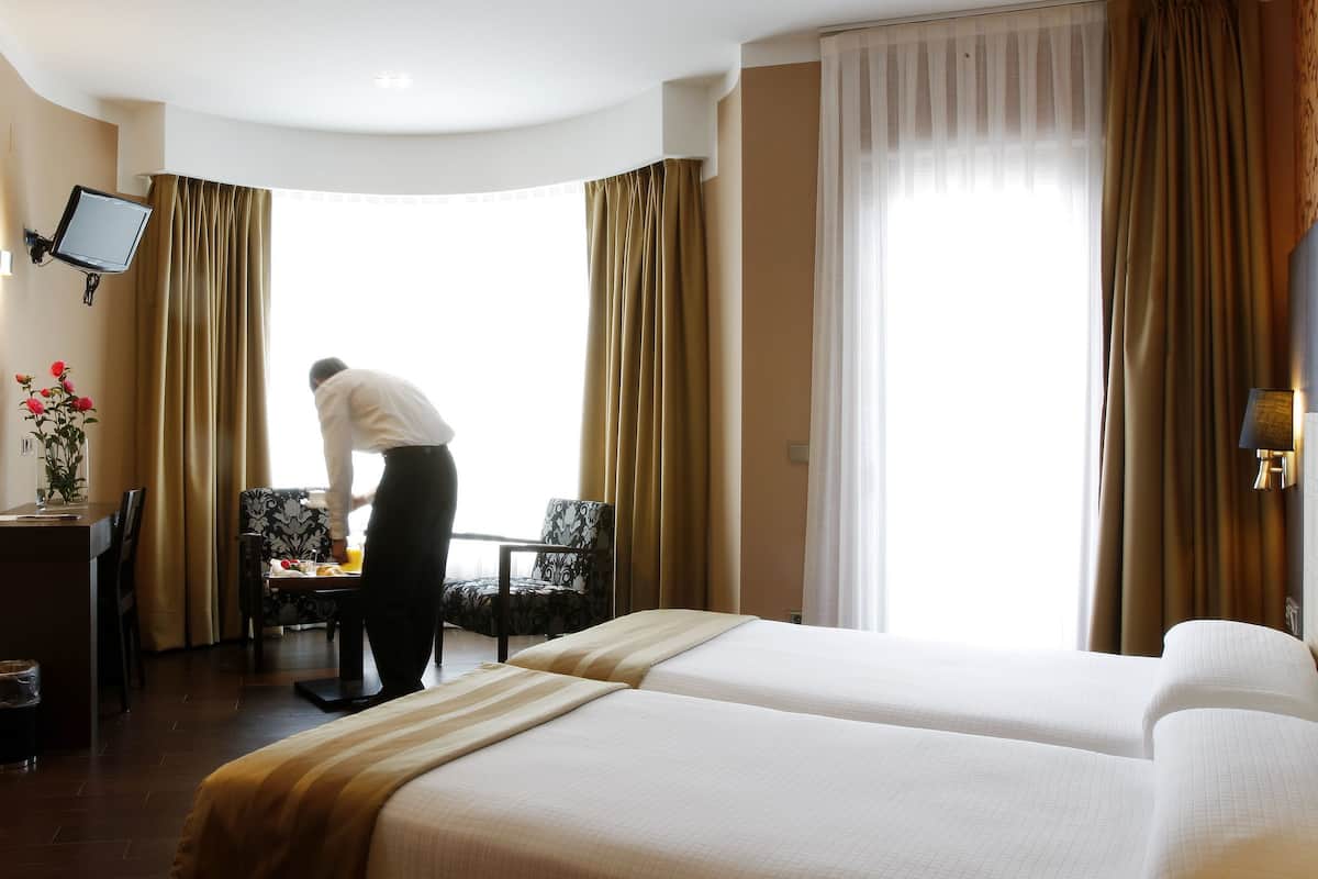 A hotel room with two beds, a desk, a chair, a TV, and a window with curtains.