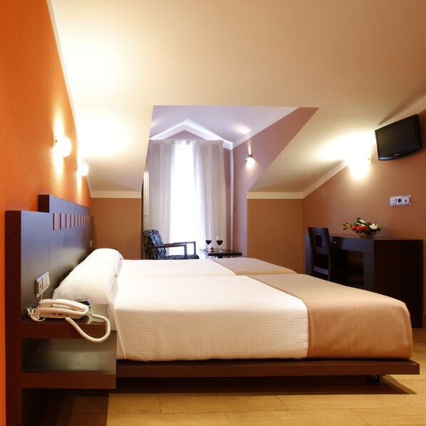 A hotel room with a bed, bedside telephone, a flat-screen TV mounted on the wall, and a small table with a vase of flowers. - Blanco Hotel Spa (Navia)