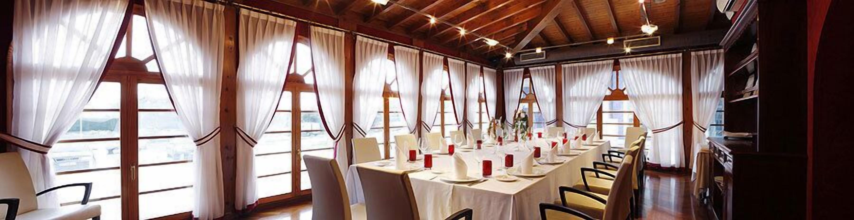 A long dining table set for a meal in a room with large windows and wooden beams.