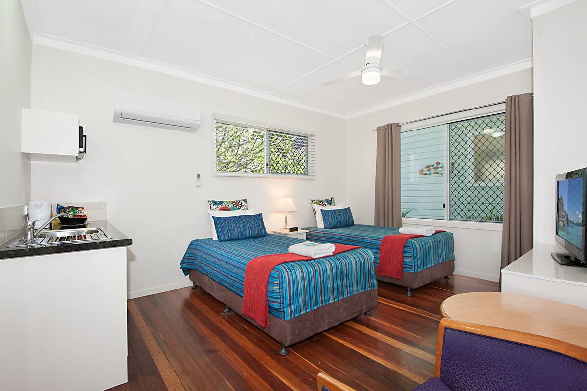Habitación de hotel con dos camas, una kitchenette pequeña, un televisor y una ventana con vistas.