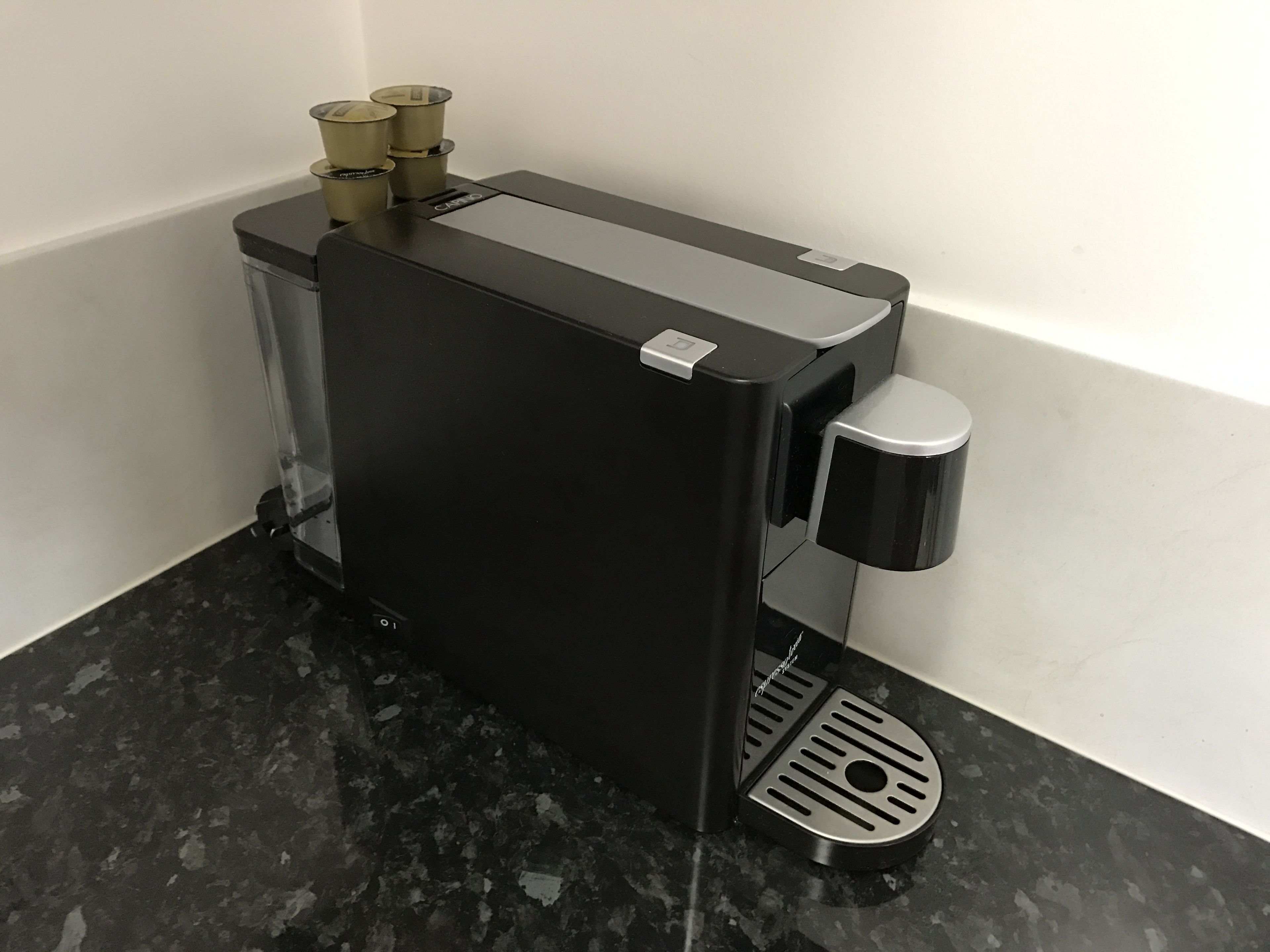 A black coffee machine with a foot pedal, a small display, and three brass knobs on top.