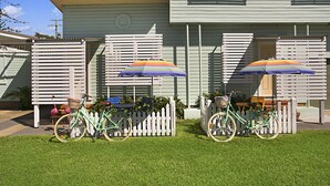 A green bicycle parked in front of a white picket fence with a colorful umbrella. - La Costa Motel (Bilinga)