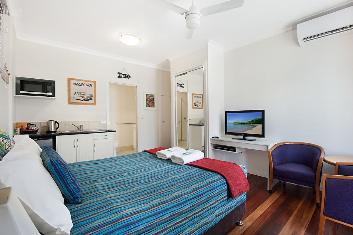 Una habitación de hotel con cama, escritorio con televisor, una silla y una kitchenette.