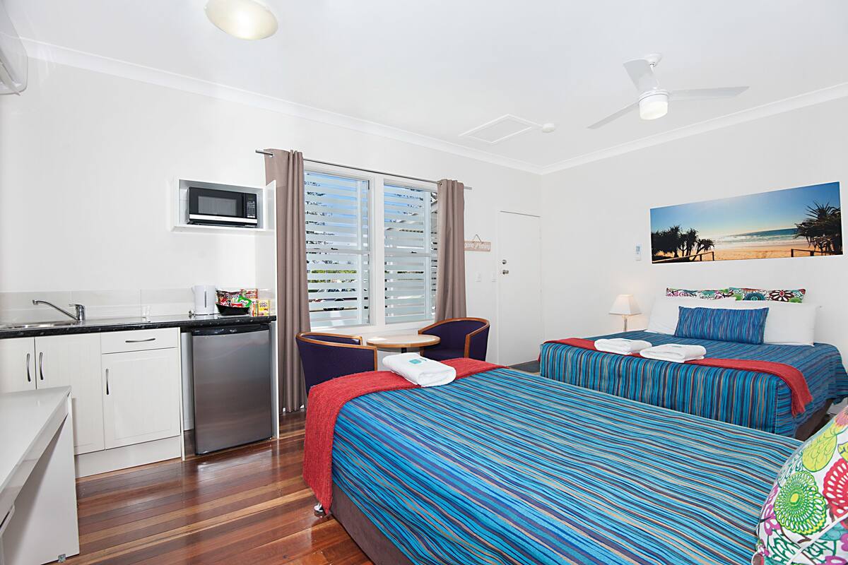 Habitación de hotel con dos camas, kitchenette, ventilador de techo y vista al mar.