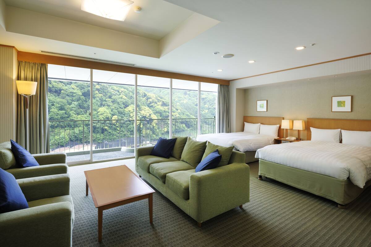 Quarto de hotel com uma grande janela, um sofá verde, uma cama e uma mesa pequena.