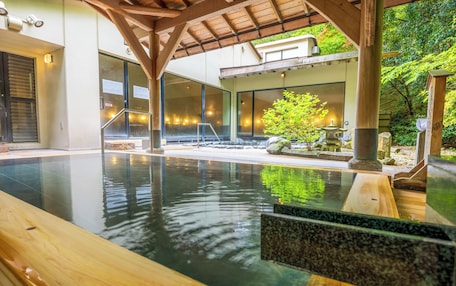 A modern indoor pool with a wooden deck, glass walls, and a stone lantern.