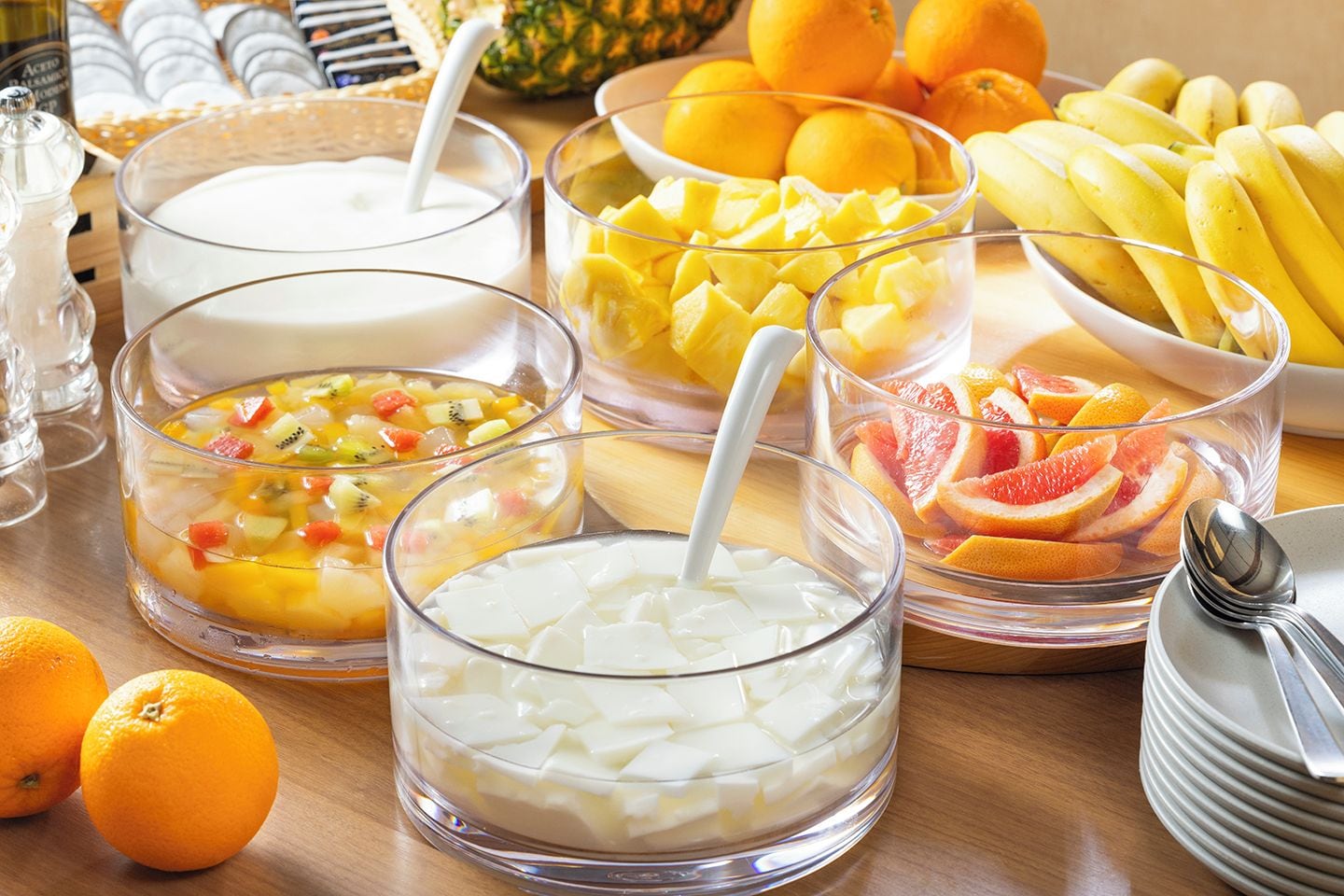 A table with various food items including bowls of yogurt, fruit, and a bowl of orange slices.