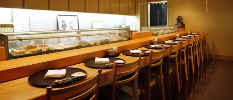 Un restaurant avec des tables et des chaises en bois, un présentoir à poissons et une fenêtre avec des rideaux.