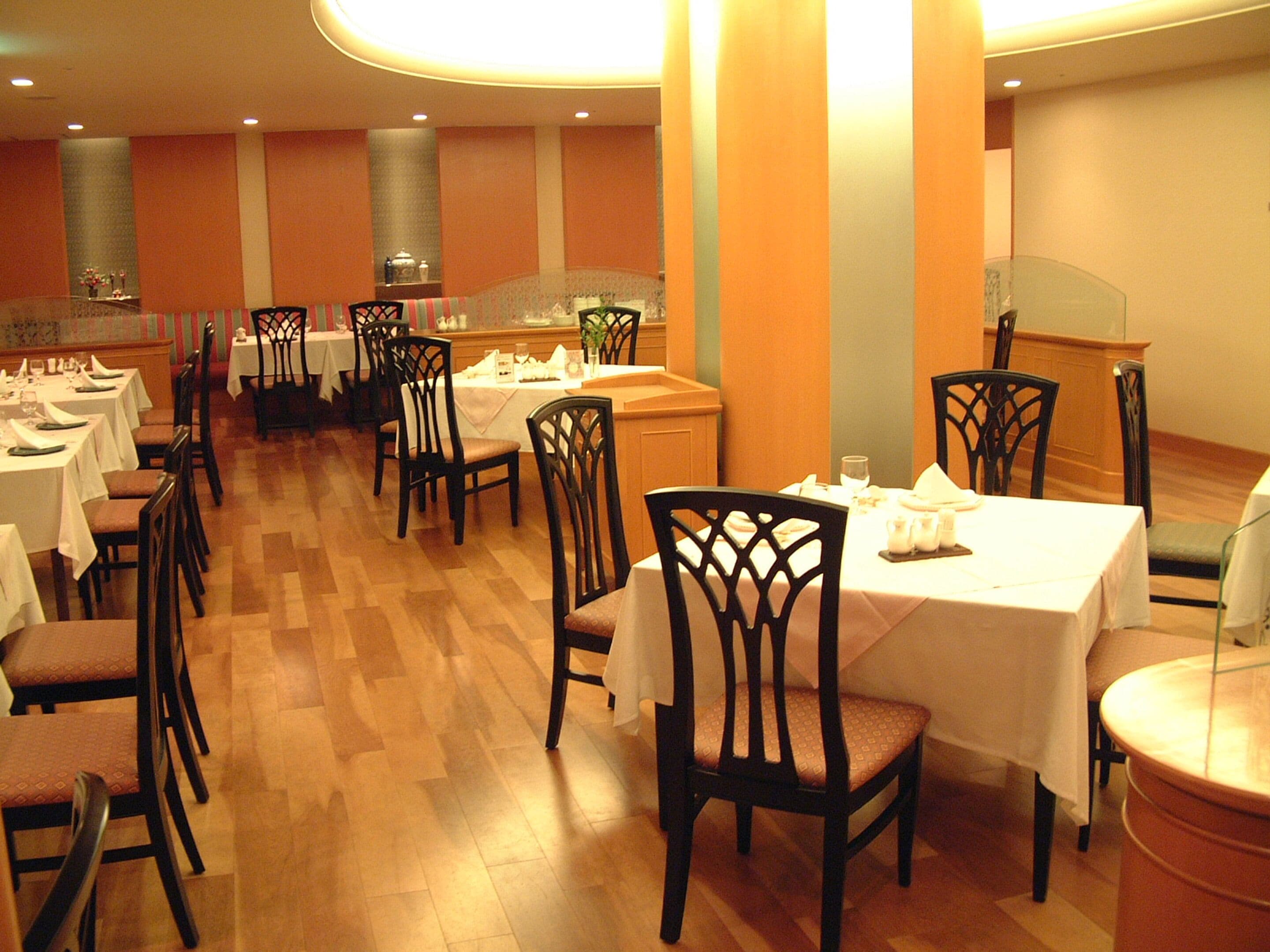 A restaurant with multiple tables and chairs, wooden flooring, and a warm color scheme.