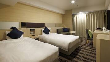 A hotel room with two beds, a desk, a chair, a small table, a TV, and a window with curtains.