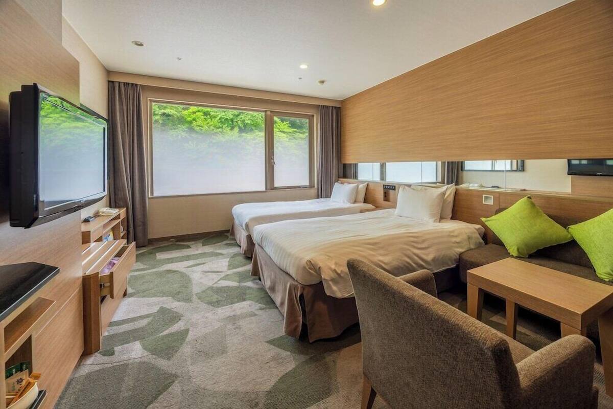 Quarto de hotel com duas camas, televisão, escrivaninha e sofá.