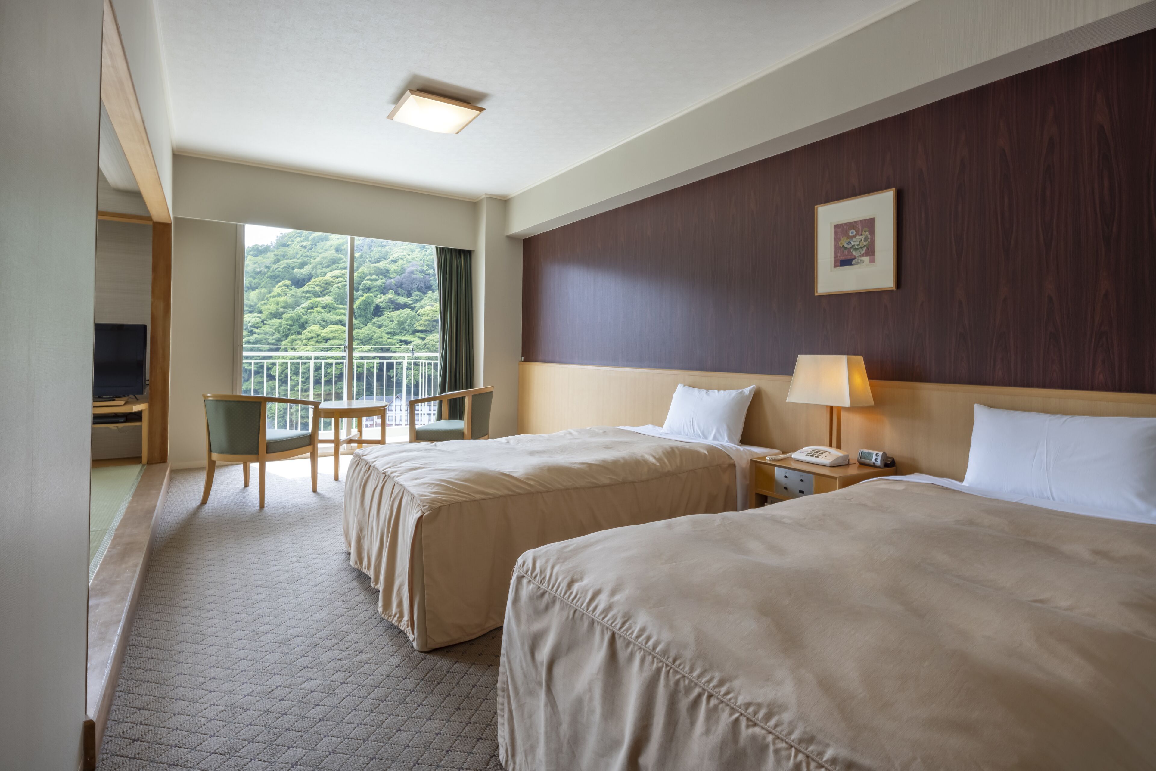 Une chambre d’hôtel avec deux lits, un bureau, une chaise et un balcon donnant sur un espace verdoyant.