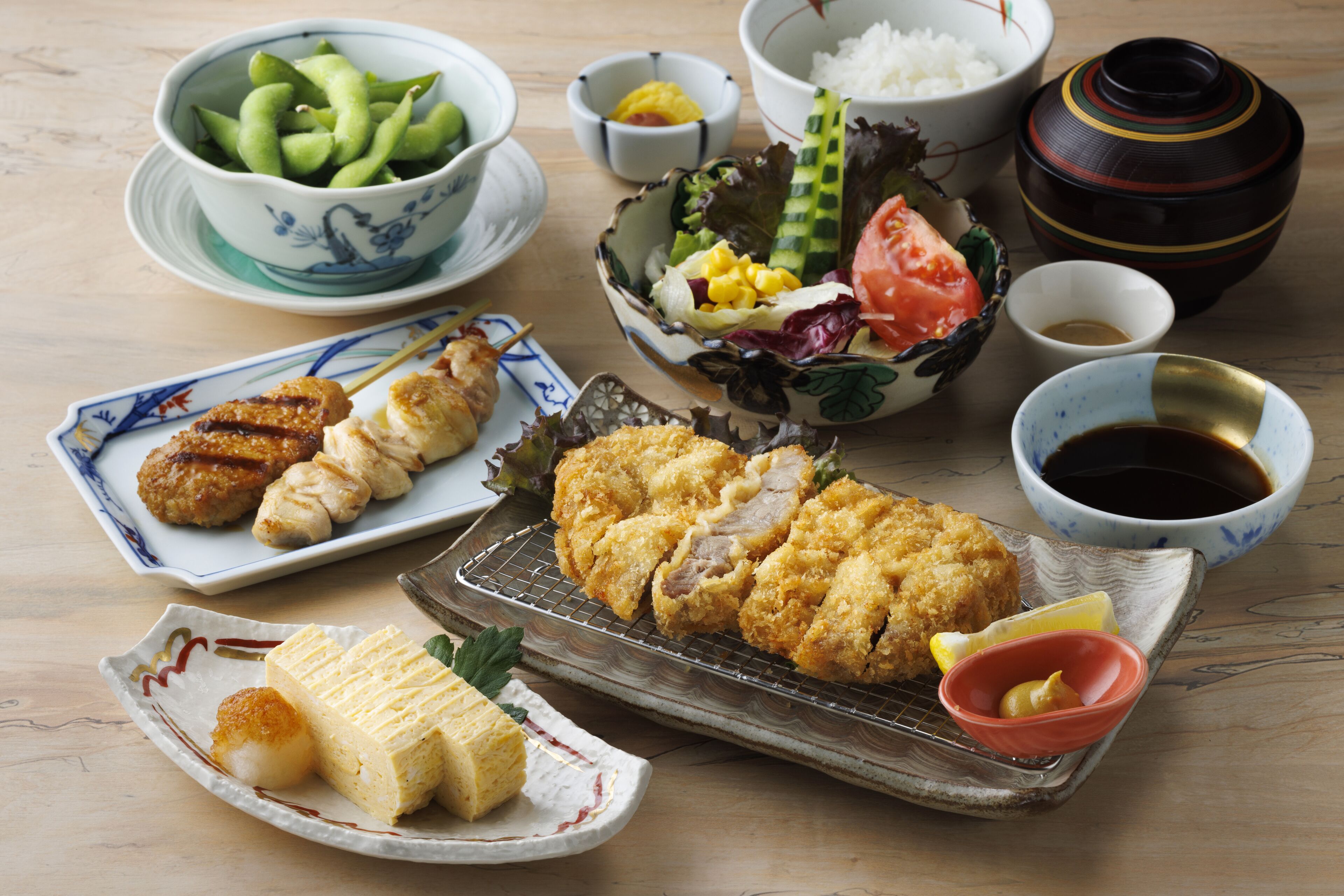 Variedad de platos japoneses, incluyendo tempura, sashimi y un tazón de edamame.
