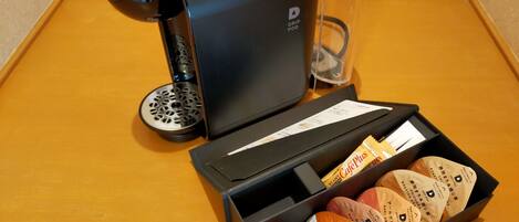 A drip coffee pod dispenser and a box of assorted coffee pods on a wooden table.