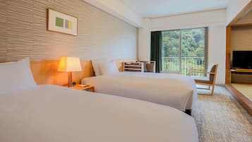 Habitación de hotel con dos camas, un escritorio, una silla, un televisor y un ventanal con vistas a árboles.