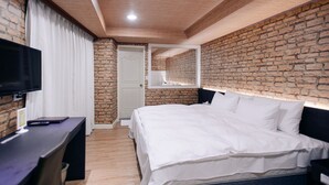 Een slaapkamer met een bakstenen muur, een houten plafond, een bed, een televisie en een bureau.